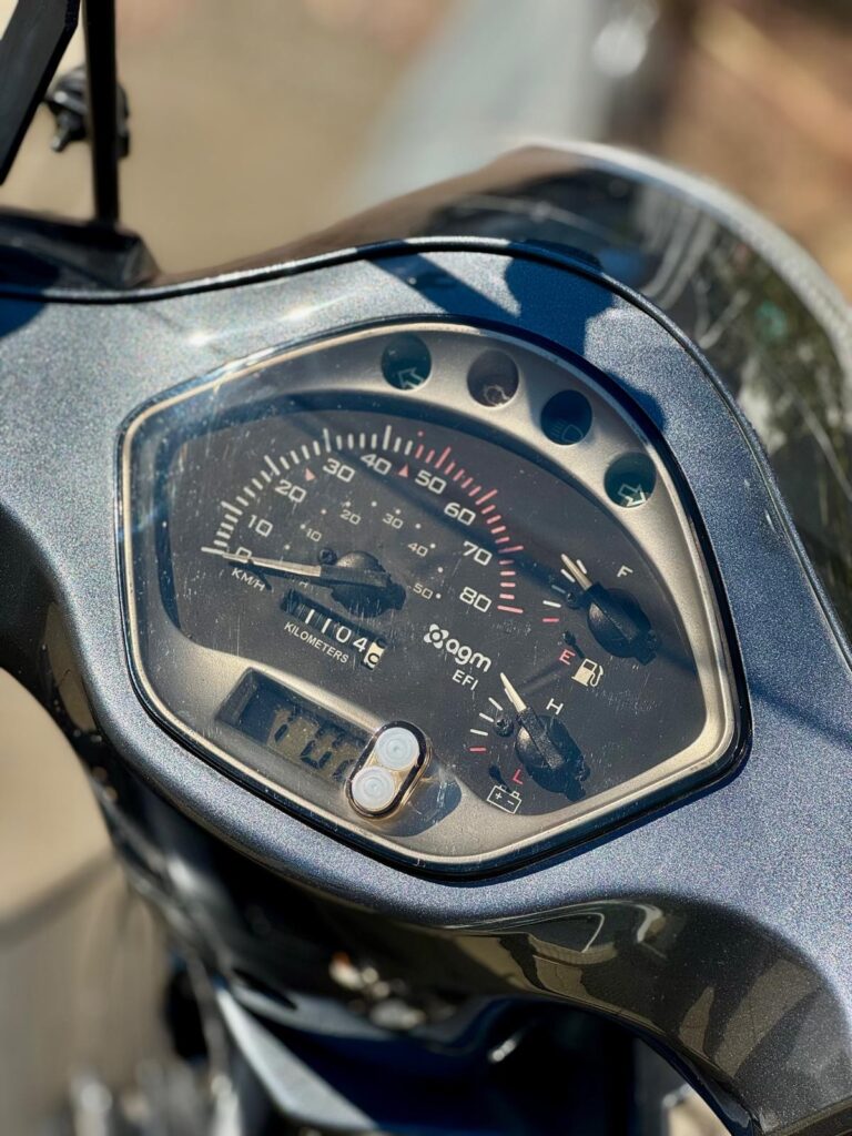Close-up van het instrumentenpaneel van een scooter met snelheidsmeter, brandstof- en temperatuurmeter.