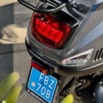 Close-up van de achterkant van een grijze scooter met rood achterlicht, LED knipperlicht en blauwe kentekenplaat.