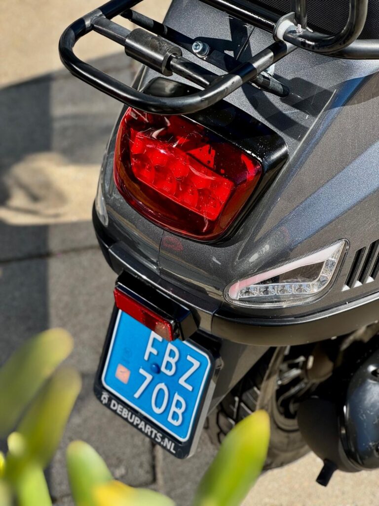Close-up van de achterkant van een grijze scooter met rood achterlicht, LED knipperlicht en blauwe kentekenplaat.