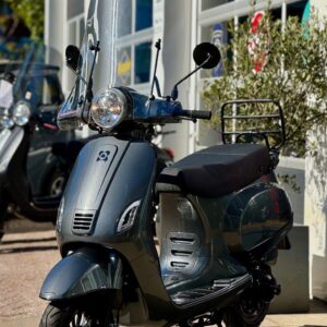 Donkergrijze scooter met hoog windscherm op de standaard, geparkeerd voor een showroom