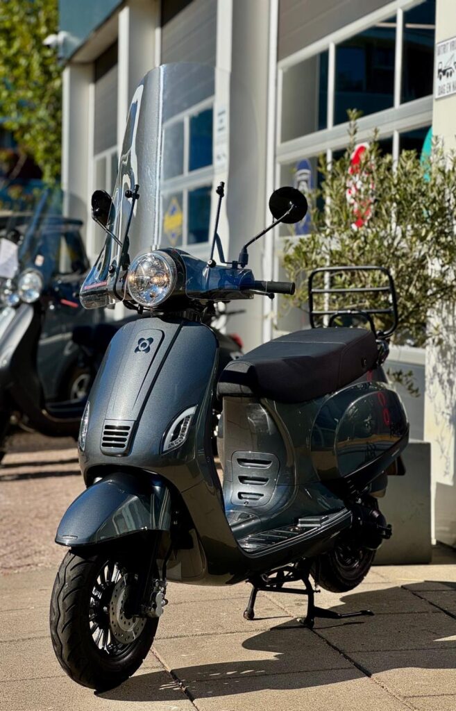 Donkergrijze scooter met hoog windscherm op de standaard, geparkeerd voor een showroom