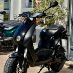 Zwarte scooter met grove banden geparkeerd buiten bij een winkel of showroom.