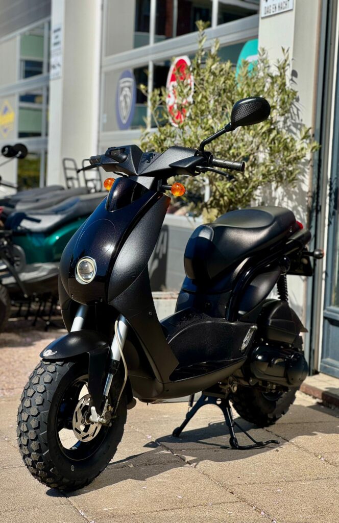 Zwarte scooter met grove banden geparkeerd buiten bij een winkel of showroom.