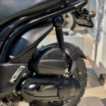 Close-up van de achterzijde van een zwarte Peugeot-scooter met vering, kentekenhouder en noppenband.