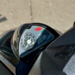 Close-up van het dashboard van een scooter met analoge snelheidsmeter en Peugeot-logo.