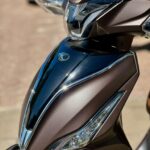 Close-up van de voorkant van een bruin metallic scooter met koplamp en windscherm.
