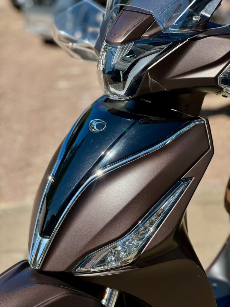 Close-up van de voorkant van een bruin metallic scooter met koplamp en windscherm.