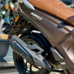 Close-up van de achterzijde van een matte bruine scooter met bruine zitting, zwart wiel en uitlaat in de zon.