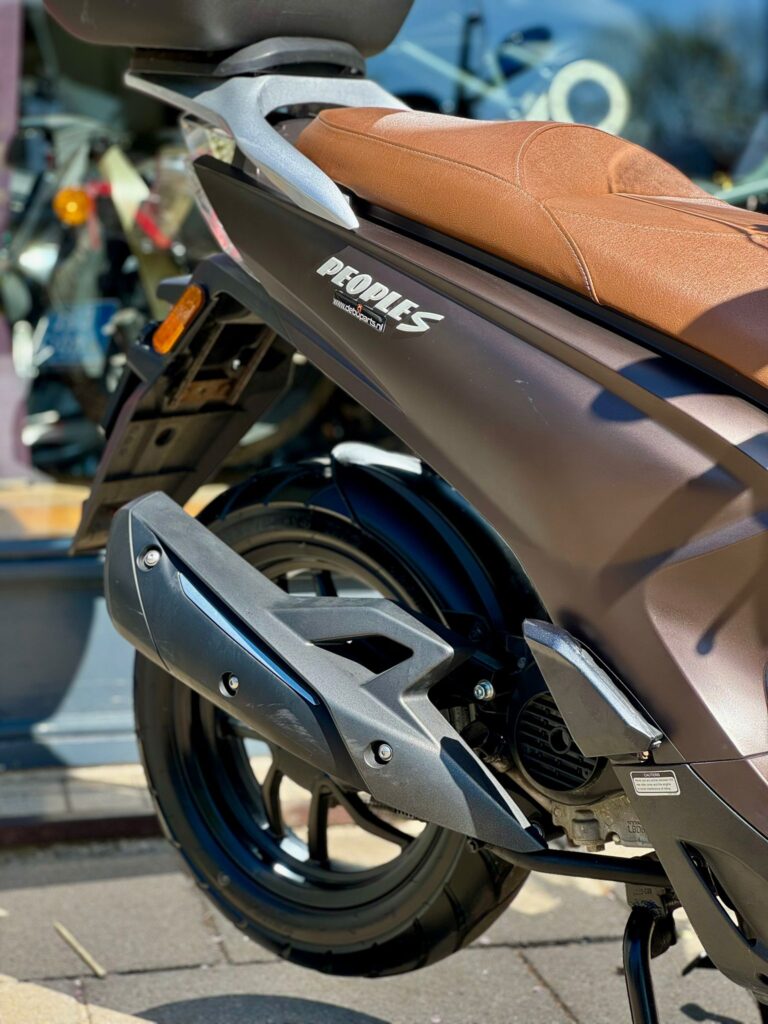 Close-up van de achterzijde van een matte bruine scooter met bruine zitting, zwart wiel en uitlaat in de zon.
