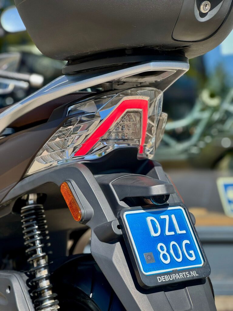 Close-up van de achterkant van een scooter met blauw NL-kenteken en LED-achterlicht.