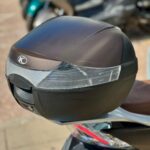 Close-up van een zwarte topkoffer op een scooter, met reflectoren en onscherpe scooters op de achtergrond.