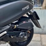 Close-up van de zijkant van een zwarte TOMOS GS03 scooter met zadel, uitlaat en achterwiel.