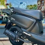 Matzwarte Tomos-scooter op de middenbok, geparkeerd voor een etalageraam.