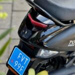 Close-up van de achterkant van een zwarte scooter met blauw kenteken en rood achterlicht.