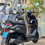 Zwarte Tomos 650S scooter met blauwe kentekenplaat, geparkeerd op de stoep bij een showroom.