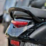 Close-up van de achterzijde van een zwarte scooter met zadel, duohandgreep en achterlicht.