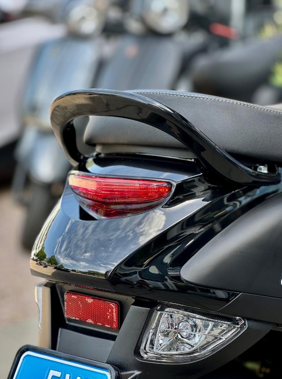 Close-up van de achterzijde van een zwarte scooter met zadel, duohandgreep en achterlicht.