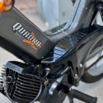 Close-up van het motorblok en frame van een zwarte Tomos Quadro brommer met voetsteun.