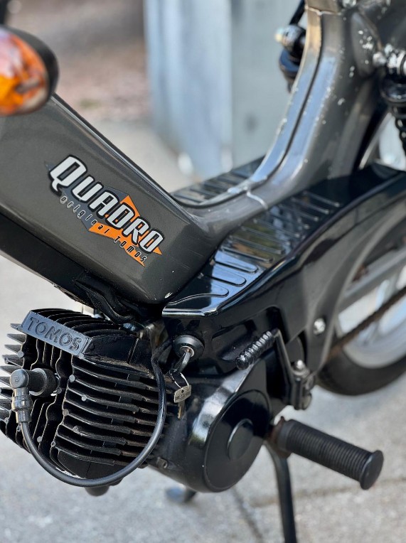 Close-up van het motorblok en frame van een zwarte Tomos Quadro brommer met voetsteun.