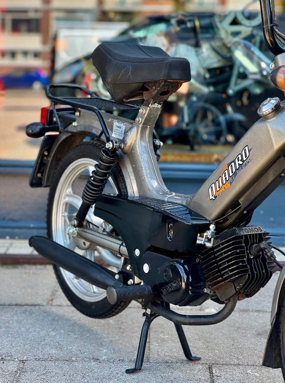Close-up van een klassieke brommer met Quadro-logo, op standaard geparkeerd op de stoep.