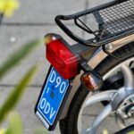 Close-up van de achterzijde van een bromfiets met bagagedrager, rood achterlicht en blauw kenteken.