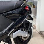 Achterzijde van een zwarte scooter met bagagedrager, geveerde achterbrug en schijfrem op de stoep.