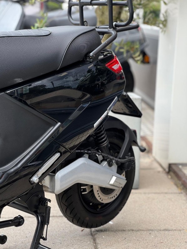 Achterzijde van een zwarte scooter met bagagedrager, geveerde achterbrug en schijfrem op de stoep.