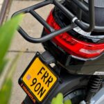 Achterkant van een zwarte scooter met stevig bagagerek, rood achterlicht en gele kentekenplaat.