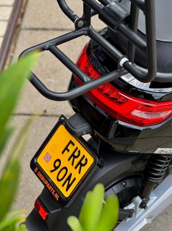 Achterkant van een zwarte scooter met stevig bagagerek, rood achterlicht en gele kentekenplaat.