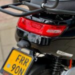 Close-up van de achterkant van een zwarte scooter met bagagedrager, rood achterlicht en gele kentekenplaat.