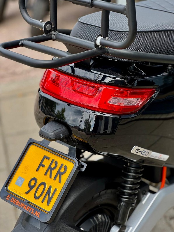 Close-up van de achterkant van een zwarte scooter met bagagedrager, rood achterlicht en gele kentekenplaat.