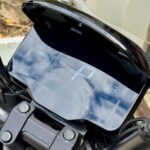 Digitaal dashboard van een motorfiets met P-indicator, batterij-icoon en stuurklem, met wolken weerspiegeld.