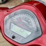 Close-up van het dashboard van een rode scooter met analoge toerenteller en digitaal scherm met 0 km/u.