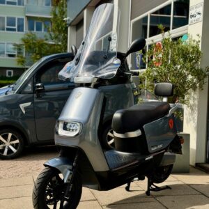 Grijze elektrische scooter met hoog windscherm, Yadea E8S, geparkeerd voor een showroom.