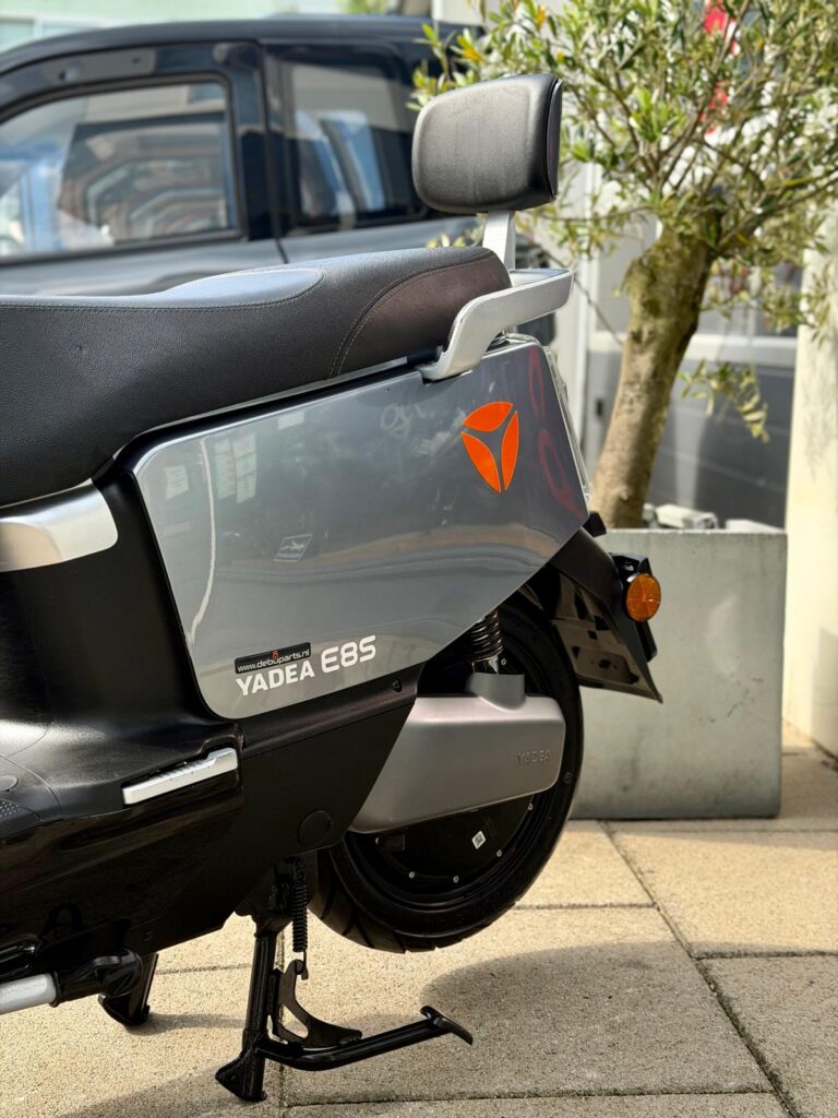 Close-up van de zijkant van een grijze Yadea E8S elektrische scooter op de middenstandaard, geparkeerd buiten.