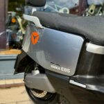 Close-up van de achterzijde van een grijze Yadea E8S elektrische scooter met zadel en rugsteun bij een winkel.