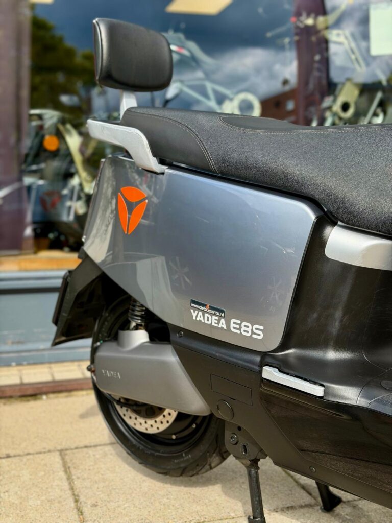 Close-up van de achterzijde van een grijze Yadea E8S elektrische scooter met zadel en rugsteun bij een winkel.