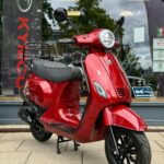 Glanzend rode scooter op de stoep, geparkeerd voor een winkel met grote ramen.