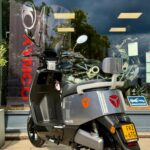 Grijze Yadea E8S elektrische scooter met windscherm en NL-kenteken voor motorzaak etalage.