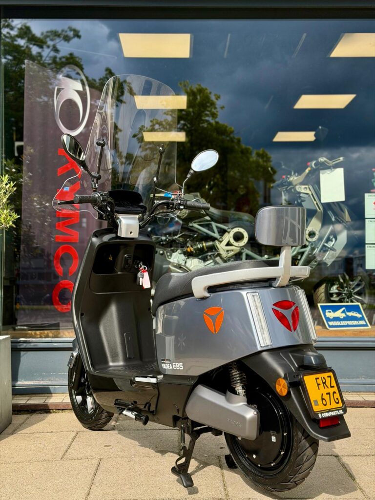Grijze Yadea E8S elektrische scooter met windscherm en NL-kenteken voor motorzaak etalage.