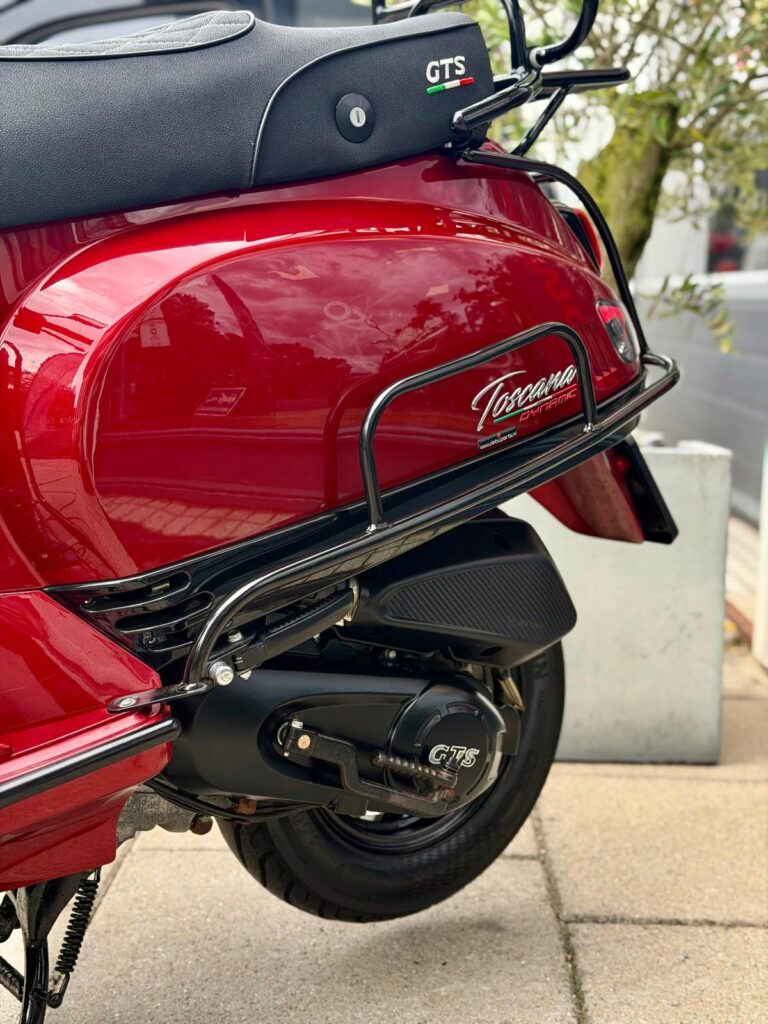 Close-up van de rode GTS-scooter: achterzijde met wiel, uitlaat en Toscana Dynamic-logo.