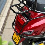 Achterzijde van een rode scooter met zwarte bagagedrager, achterlicht en gele NL-kentekenplaat.