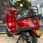 Rode retro scooter met bagagedrager en NL-kenteken, geparkeerd voor een winkelraam met reflecties