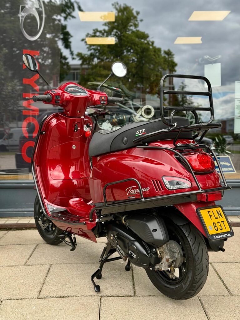 Rode retro scooter met bagagedrager en NL-kenteken, geparkeerd voor een winkelraam met reflecties