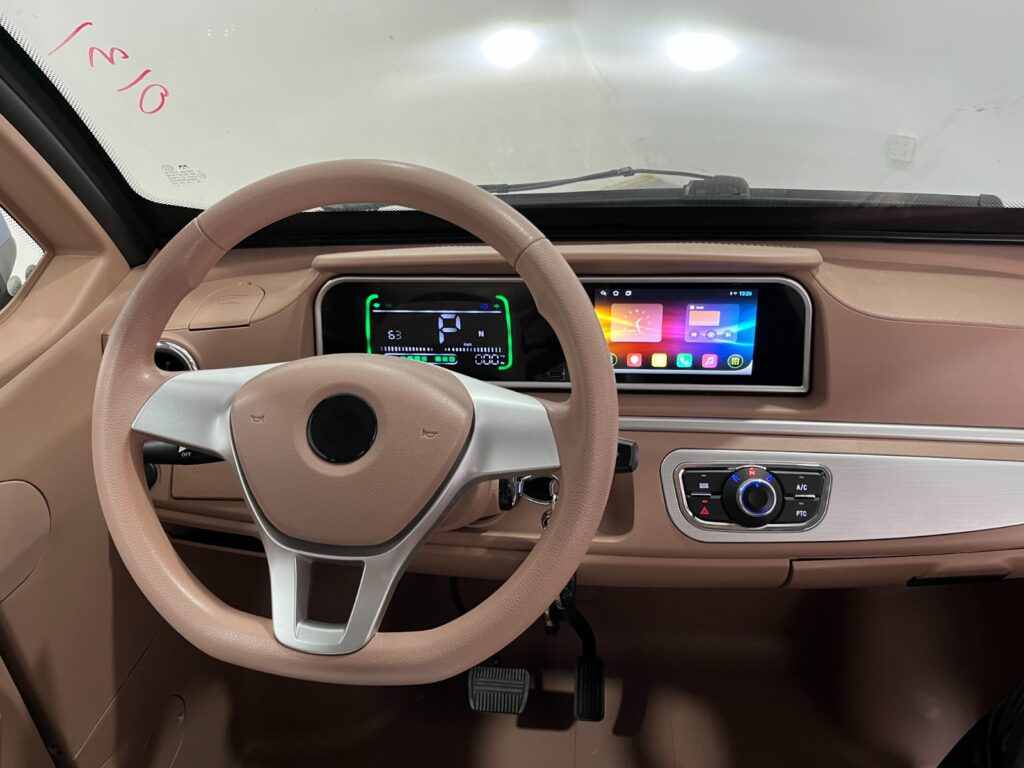 Beige autointerieur met stuur, digitaal dashboard en breed infotainmentscherm.