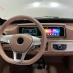 Beige autointerieur met stuur, digitaal dashboard en breed infotainmentscherm.