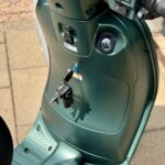 Close-up van een groene scooter met sleutels in het contact en het voetgedeelte zichtbaar.