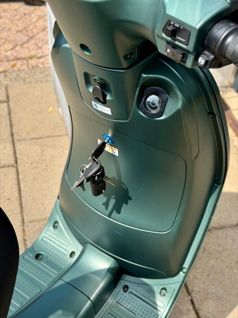 Close-up van een groene scooter met sleutels in het contact en het voetgedeelte zichtbaar.