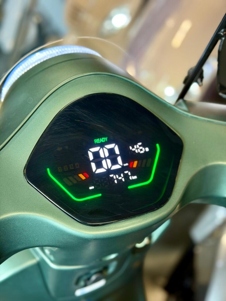 Digitaal dashboard van een elektrische scooter met snelheidsmeter en groene LED-indicatoren.