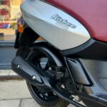 Close-up van de achterzijde van een scooter met rood zadel en zwarte uitlaat.